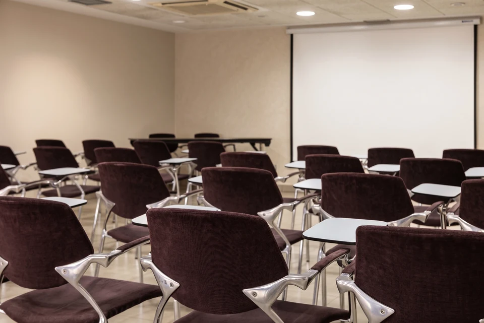 Sala Viena + Capellanes en montaje escuela, con sillas tapizadas y pantalla de proyección, en Suites Viena, Madrid centro