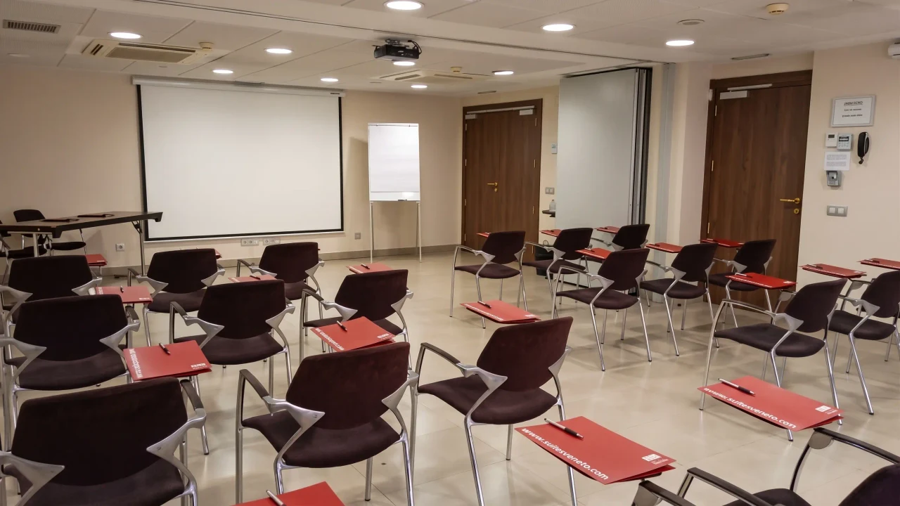 Sala Viena + Capellanes preparada para una formación, con sillas de pala, carpetas, pantalla y rotafolio, en Madrid centro